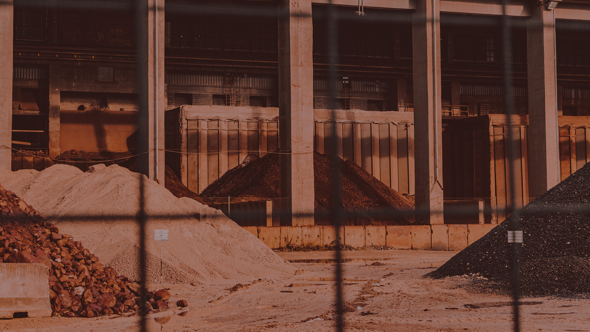 Industrial site with stockpiled materials viewed through a chain-link fence